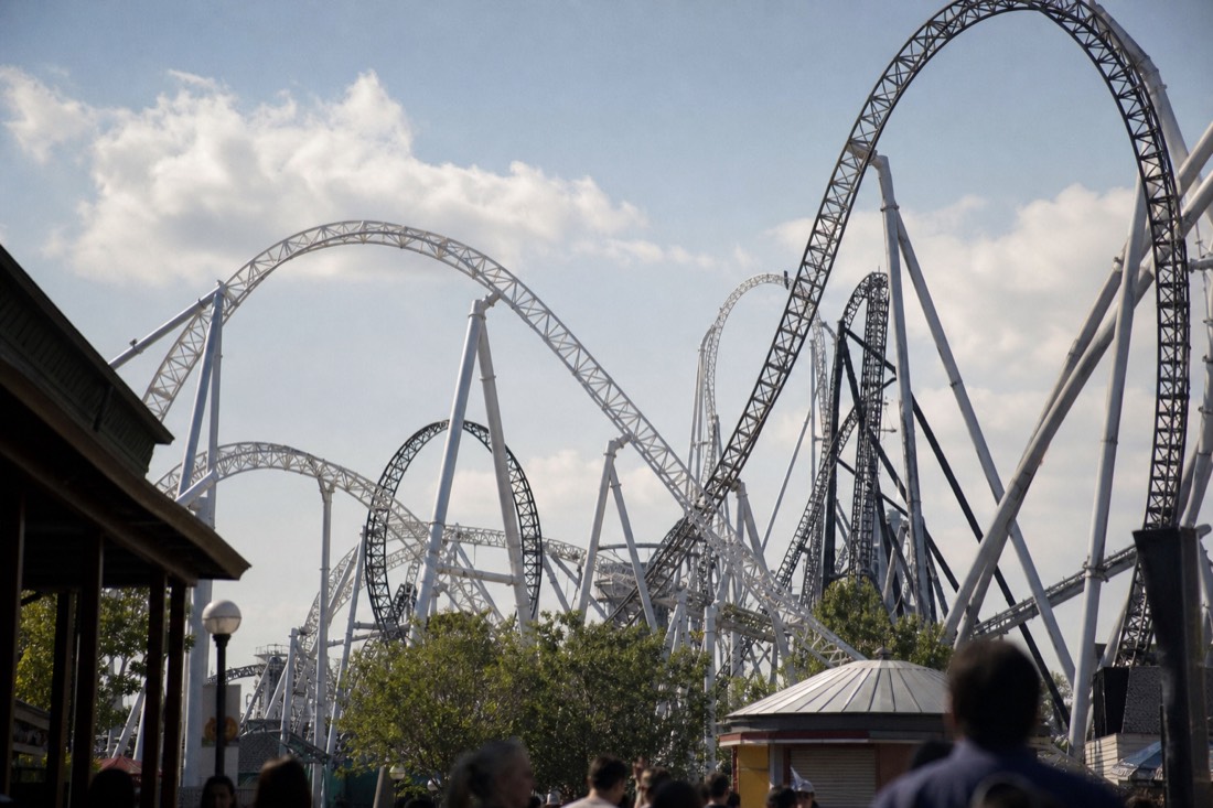 Multiple intertwining steel coaster tracks rising above a theme park on a clear morning, no riders or signage visible
