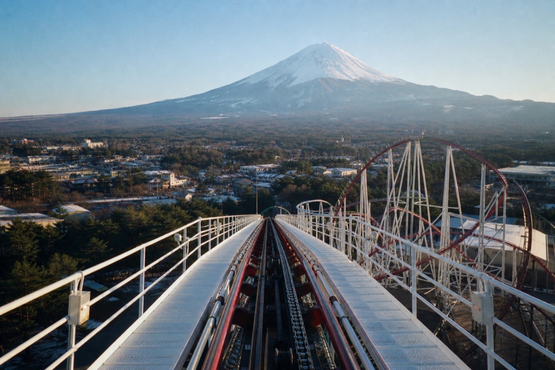 View along a tall steel coaster's lift hill toward Mount Fuji's snow-capped summit on a clear morning